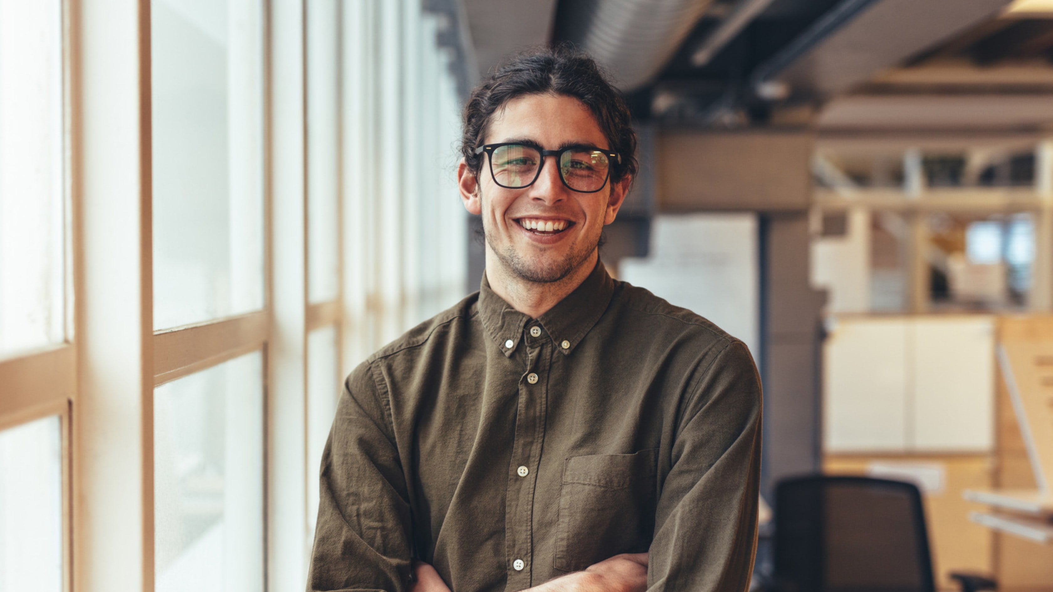 Smiling professional with glasses standing by a bright window